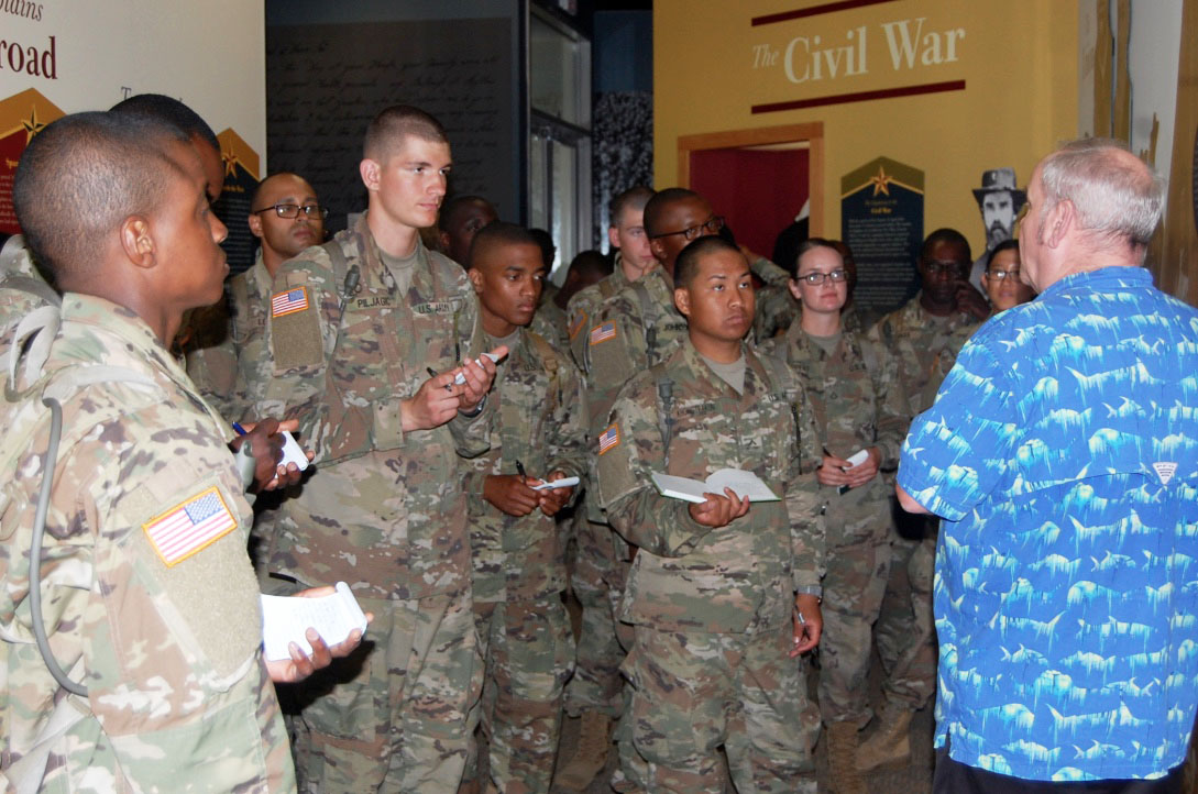 A group of Soldiers listening to a man speak inside the US Army Chaplain Corps Museum.